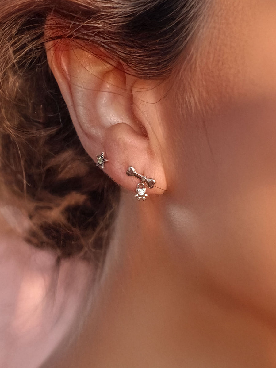 Pendientes pequeños de plata con diseño de huella y hueso en modelo.